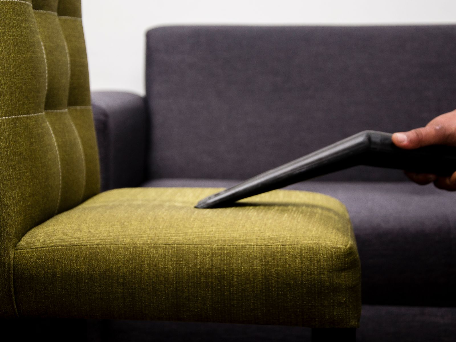A cleaner drawing a vacuum head across the upholstery of an armchair